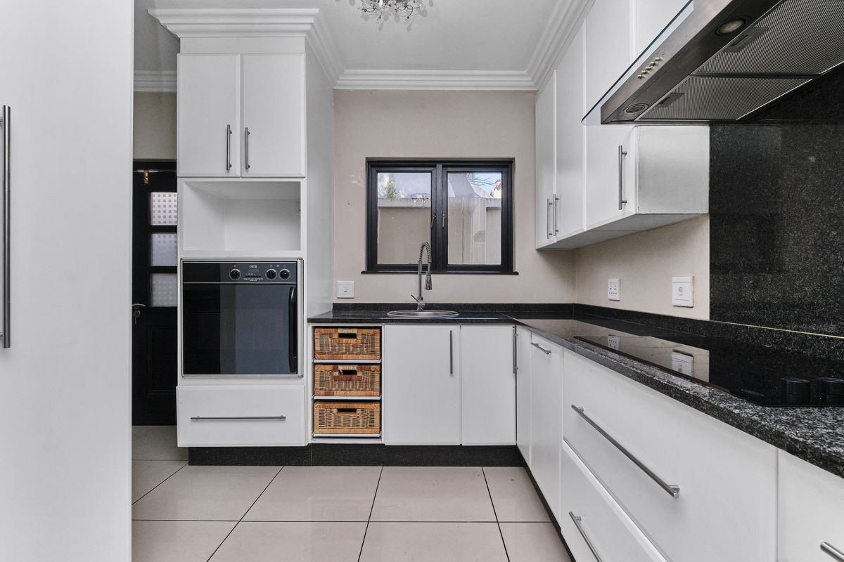 Modern kitchen featuring white cabinetry, granite countertops, built-in oven, hob, extractor fan, and tiled flooring.