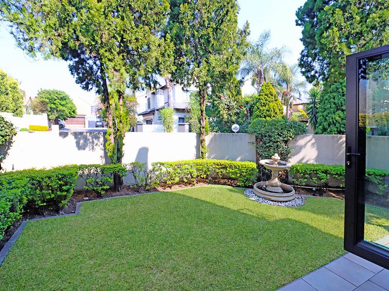A well-maintained private garden featuring a manicured lawn, established hedging, a decorative water fountain, and a secure boundary wall.