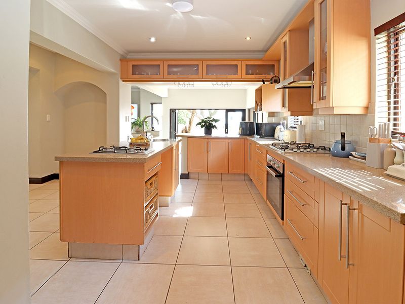 Spacious kitchen featuring light wood cabinetry, stone countertops, a central island with a gas hob, and tiled flooring throughout.