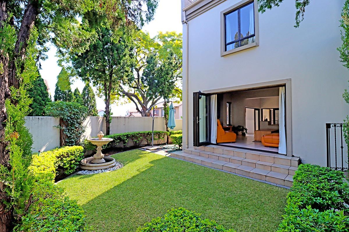 A well-maintained rear garden featuring a stone fountain, manicured lawn, and bi-fold doors providing seamless access to the interior living space.