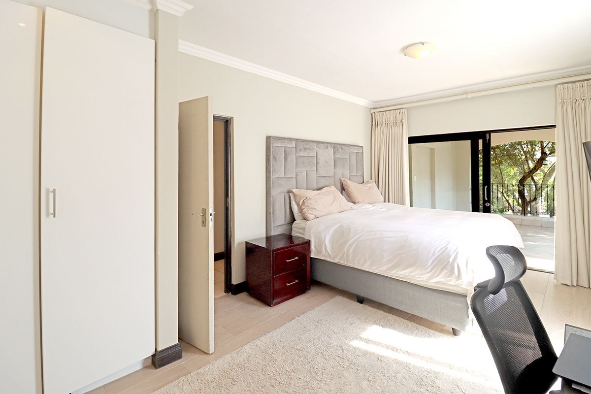 A well-lit bedroom featuring built-in wardrobes, laminate flooring, and sliding glass doors providing access to an outdoor balcony area.