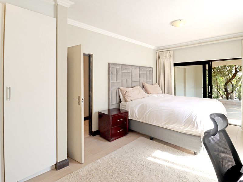 A well-lit bedroom featuring built-in wardrobes, laminate flooring, and sliding glass doors providing access to an outdoor balcony area.