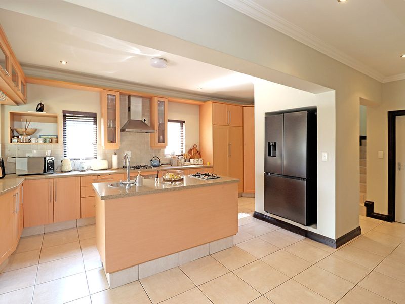 A functional kitchen featuring light wood cabinetry, stone countertops, a central island with a gas hob, and tiled flooring throughout.