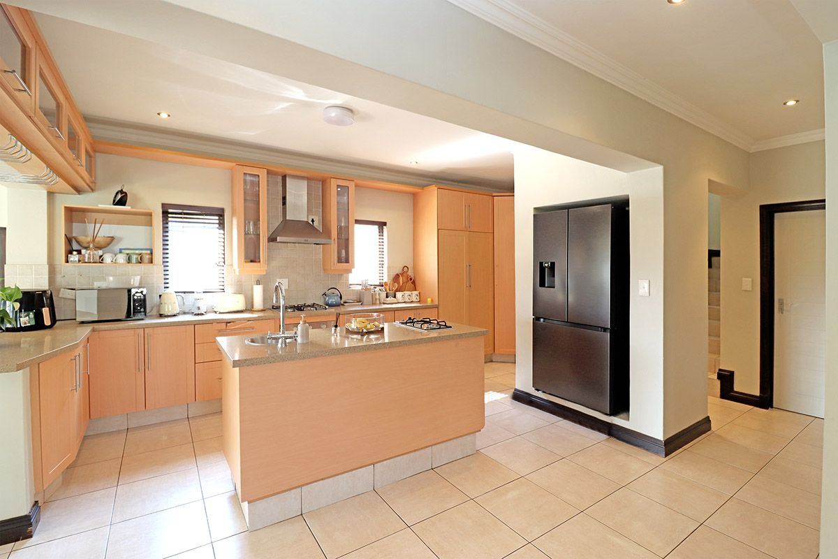 A functional kitchen featuring light wood cabinetry, stone countertops, a central island with a gas hob, and tiled flooring throughout.