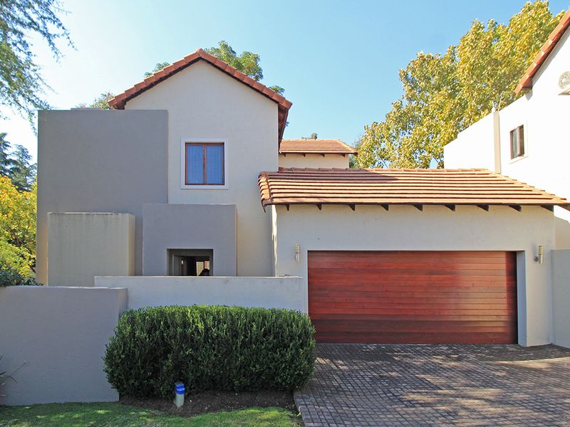 Front elevation of a two-story house featuring a tiled roof, plastered exterior walls, and a wooden garage door with a paved driveway.