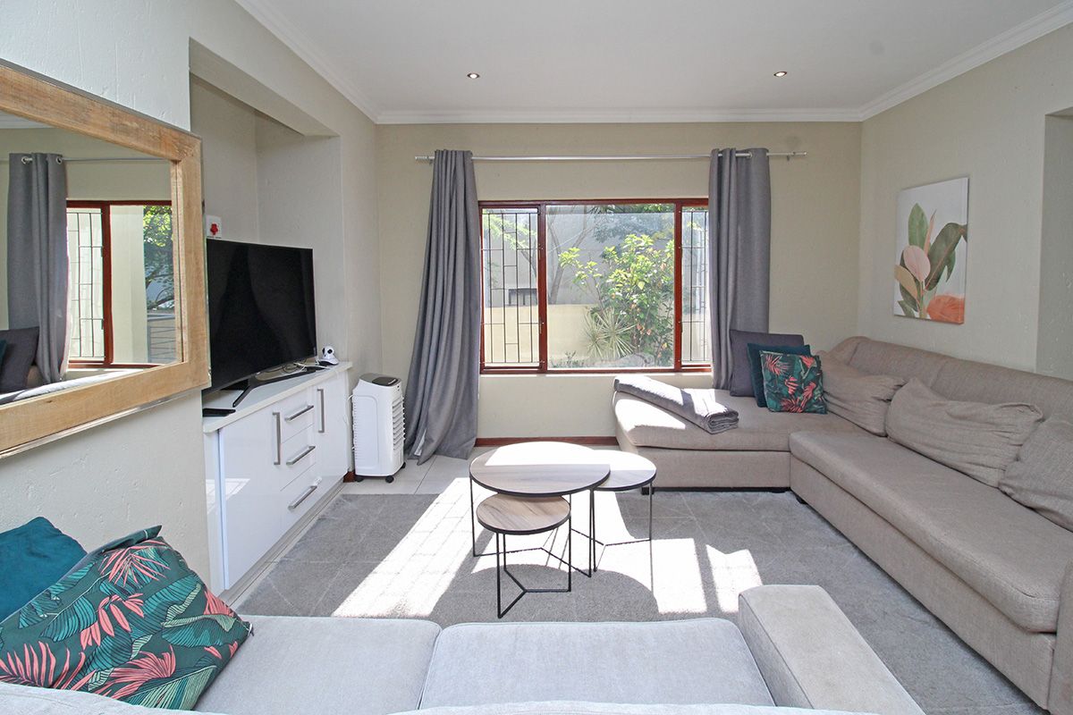 A comfortable living room featuring recessed downlights, built-in cabinetry, and a large window with security bars, providing a bright and functional space.