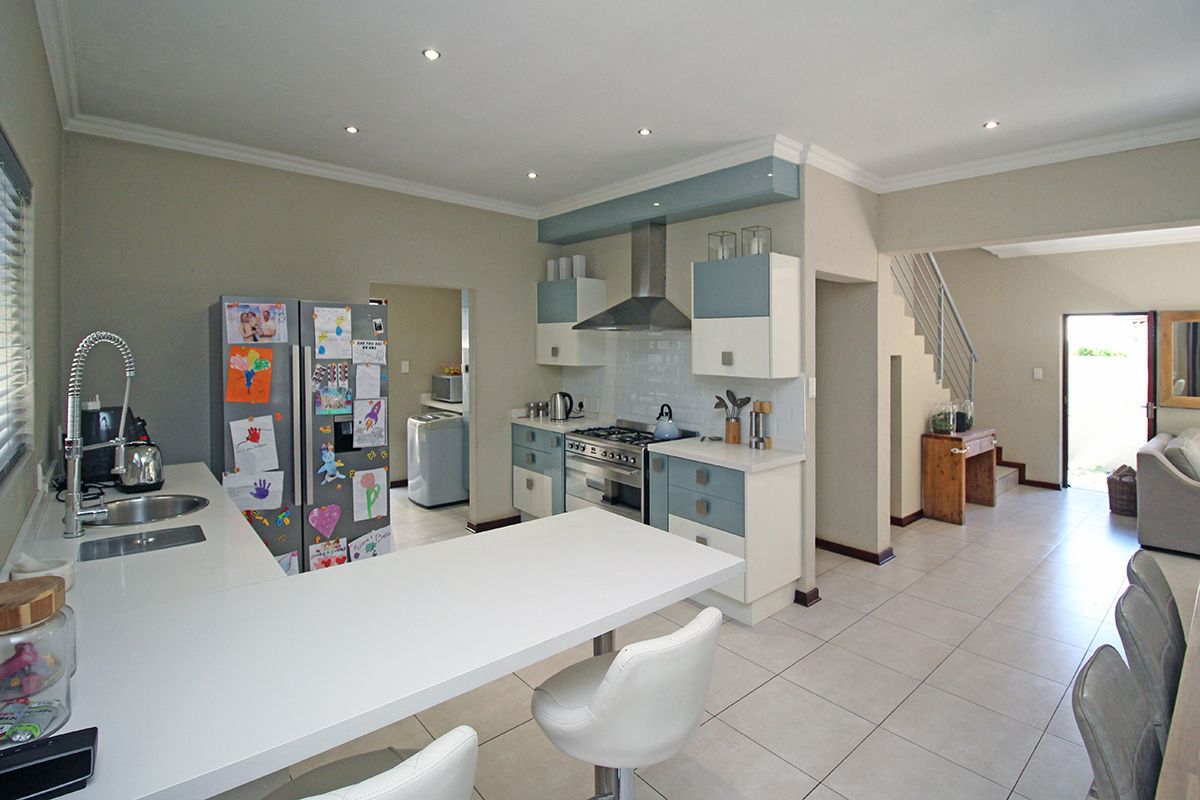 Modern kitchen featuring a gas hob, extractor fan, built-in oven, and a breakfast bar, seamlessly connected to the living area and staircase.