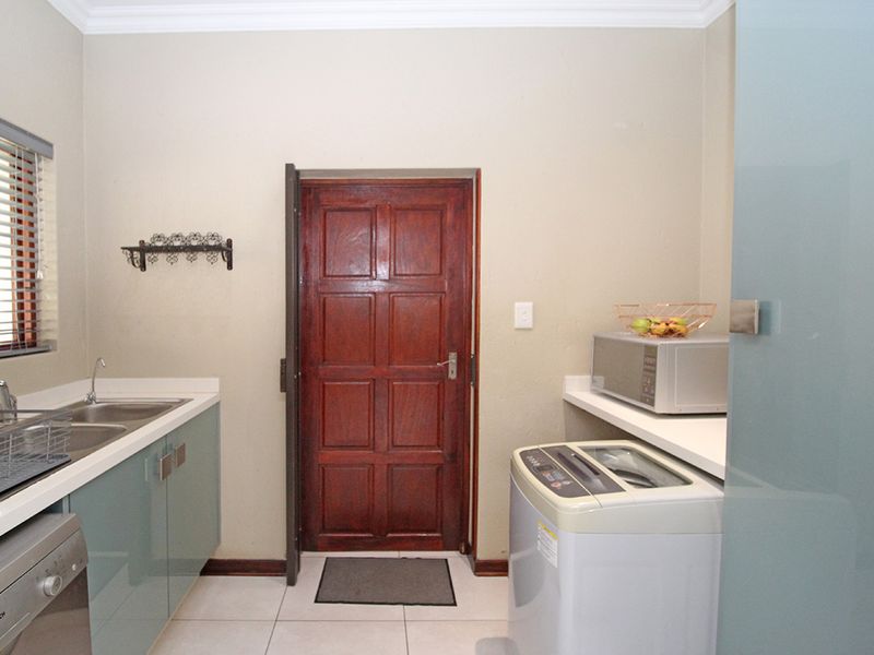 A functional laundry room featuring built-in cabinetry, double stainless steel sink, tiled flooring, and direct access via a solid timber door.