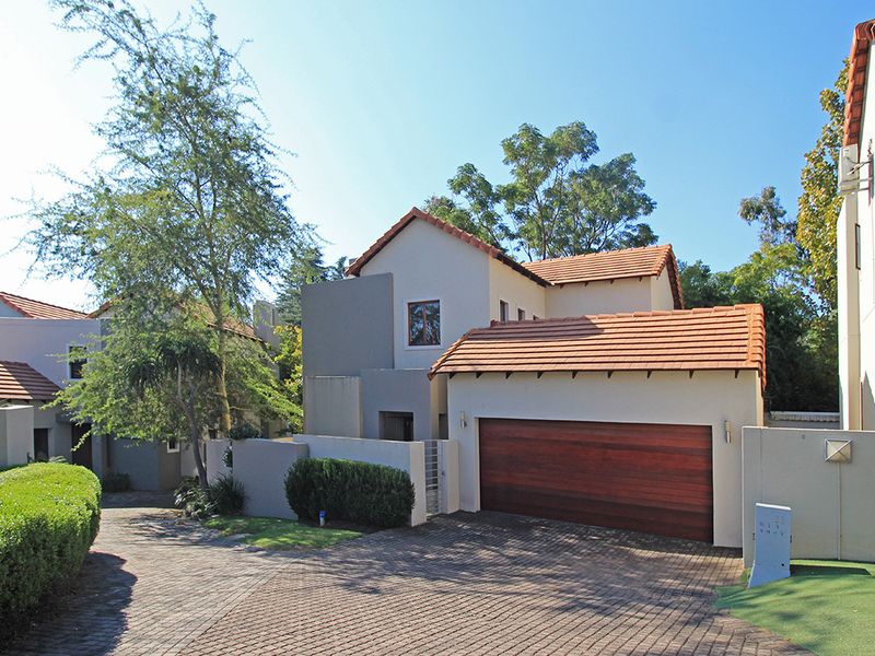 Front elevation of a residential house featuring a tiled roof, a wooden garage door, and a paved driveway within a landscaped complex.