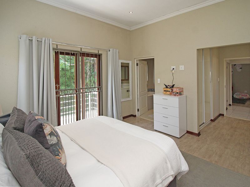 A well-lit bedroom featuring laminate flooring, built-in cupboards, and a sliding glass door with security gate leading to an outdoor area.