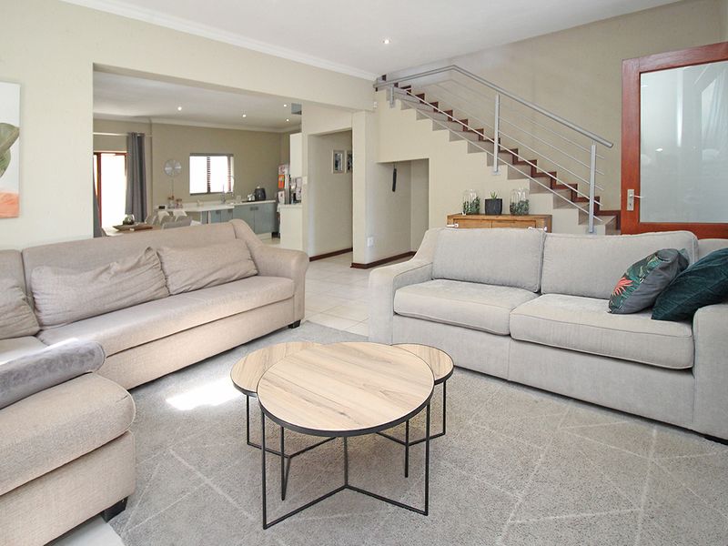 Spacious open-plan living area featuring tiled flooring, a modern staircase with metal balustrades, and seamless flow into the adjacent kitchen and dining space.