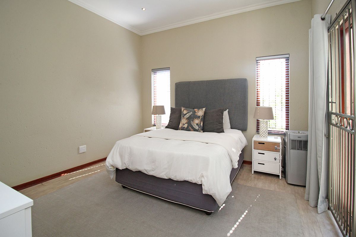 A well-maintained bedroom featuring laminate flooring, recessed downlights, and dual windows with venetian blinds, providing access to an outdoor area via a security gate.