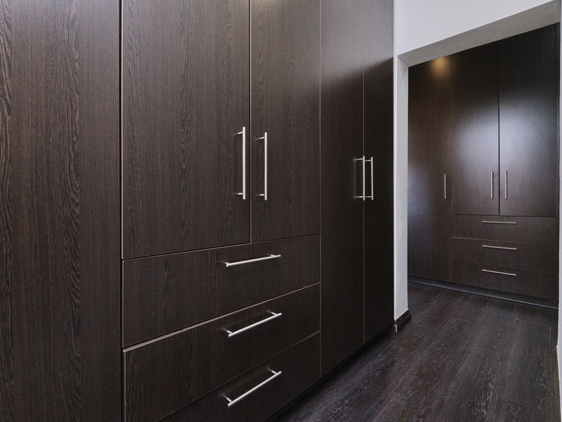 A clean, modern walk-in closet or bedroom area featuring extensive dark wood built-in cabinetry with integrated drawers and matching laminate flooring.