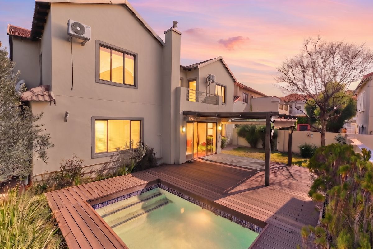 Rear view of the property featuring a swimming pool, timber decking, pergola, and a balcony, set against a sunset sky.