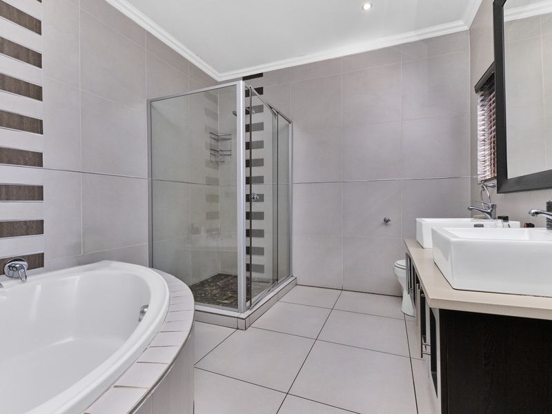 Modern bathroom featuring a built-in bathtub, glass shower enclosure, and a double vanity with vessel sinks, finished with neutral wall and floor tiles.