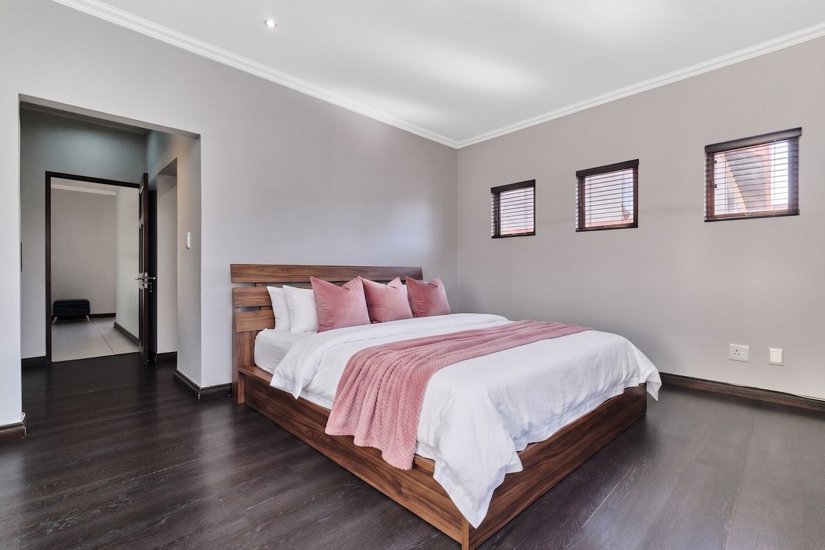 A well-maintained bedroom featuring dark wood laminate flooring, neutral wall tones, recessed lighting, and fitted venetian blinds.