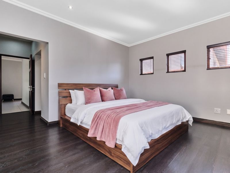 A well-maintained bedroom featuring dark wood laminate flooring, neutral wall tones, recessed lighting, and fitted venetian blinds.