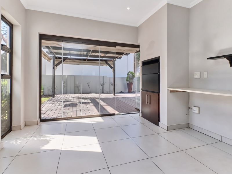 Bright living area featuring tiled floors, a built-in braai, and large sliding glass doors opening onto a wooden deck patio.