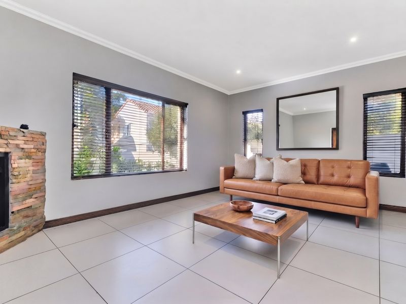 A bright living room featuring large windows with venetian blinds, neutral tiled flooring, and a distinctive stone-clad fireplace.
