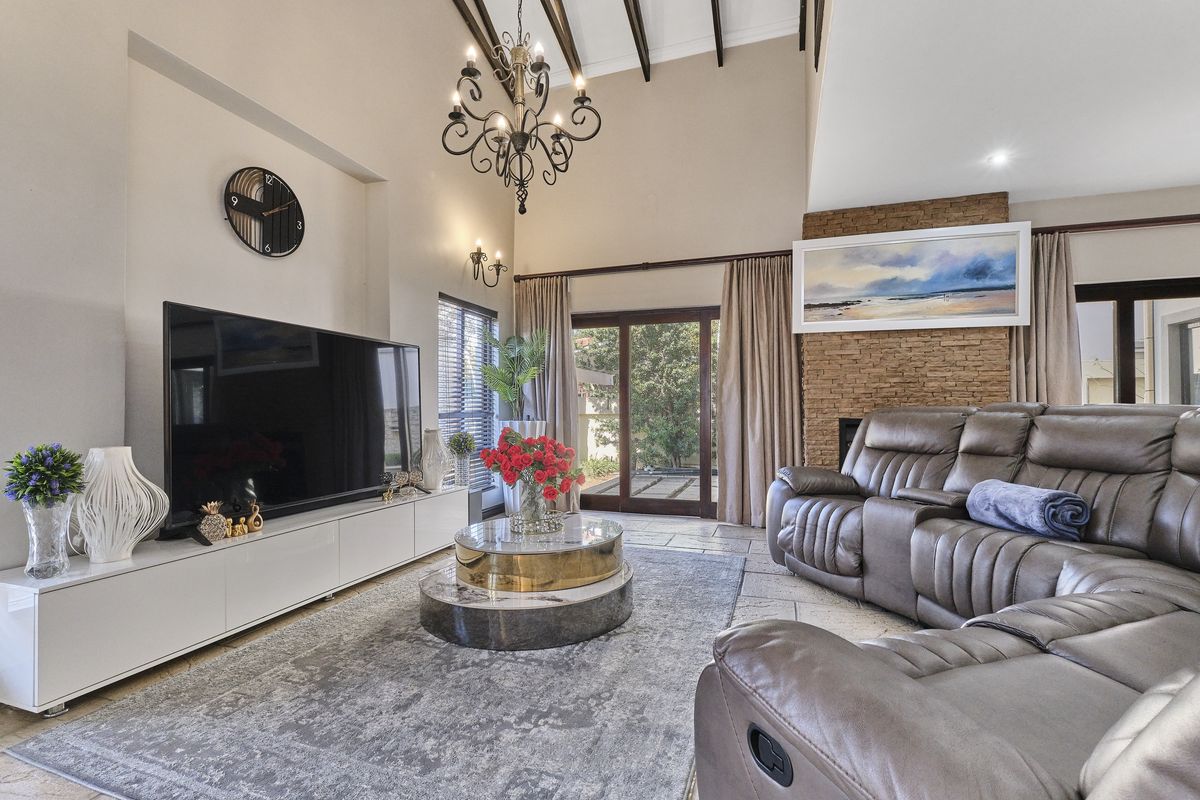 Spacious living room featuring a vaulted ceiling with exposed timber beams, a stone-clad fireplace, and large sliding glass doors leading to the outdoors.