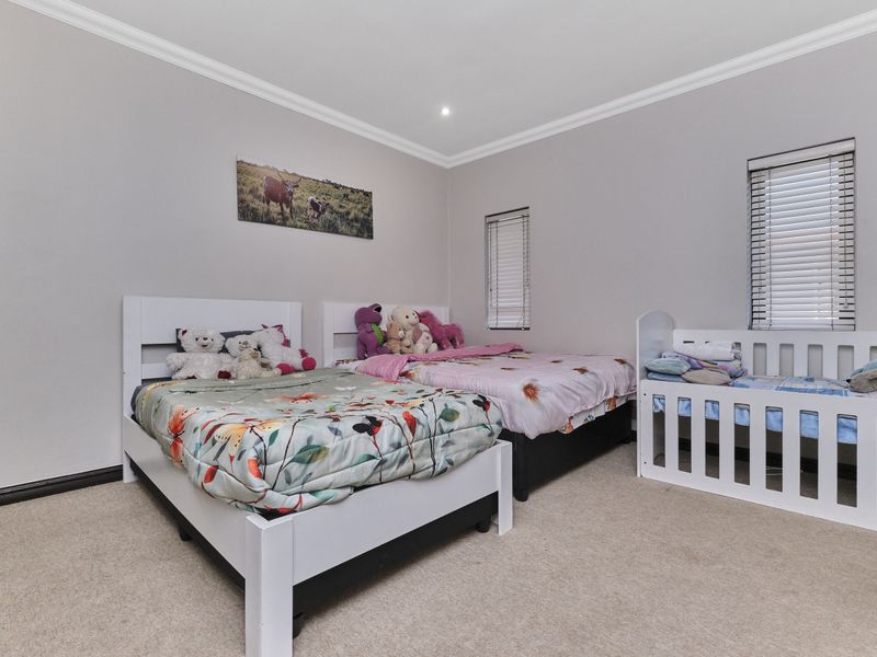 A spacious bedroom featuring neutral wall tones, carpeted flooring, and dual windows fitted with venetian blinds.
