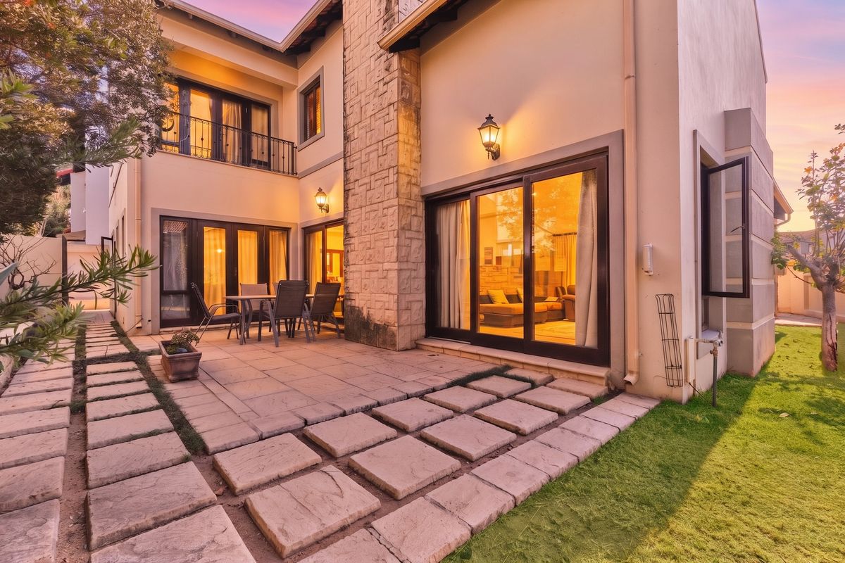 Rear view of a two-story house featuring a paved patio, stone-clad chimney, and sliding glass doors leading into the living area.