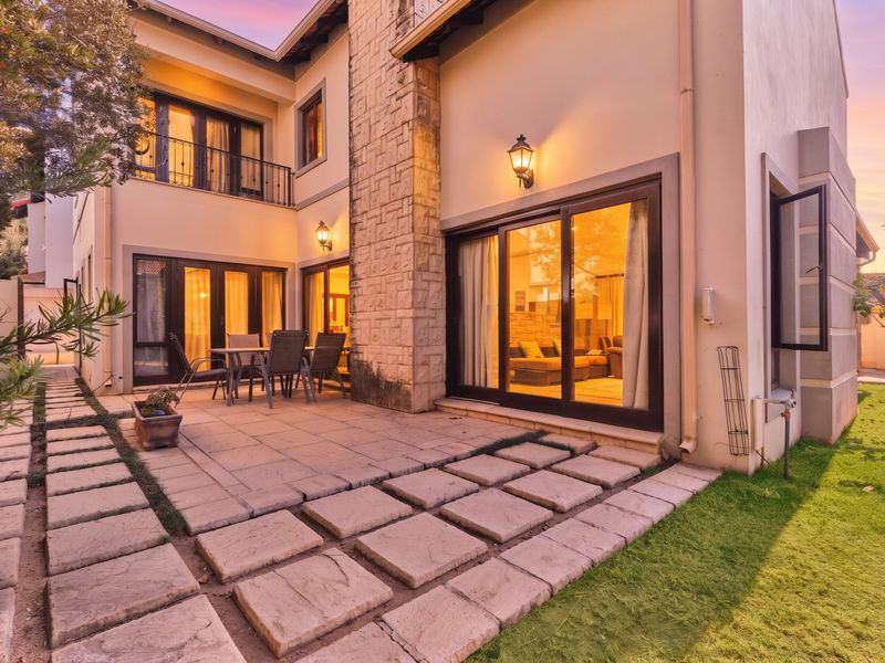 Rear view of a two-story house featuring a paved patio, stone-clad chimney, and sliding glass doors leading into the living area.