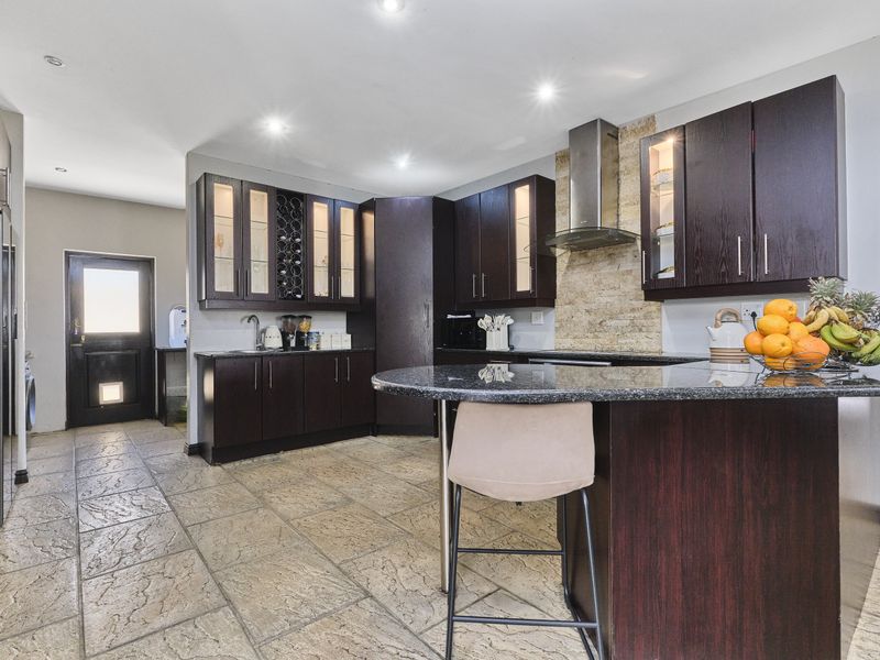 Modern kitchen featuring dark wood cabinetry, granite countertops, a breakfast bar, and stone tile flooring with integrated stainless steel extractor fan.