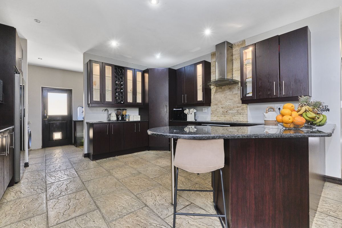 Modern kitchen featuring dark wood cabinetry, granite countertops, a breakfast bar, and stone tile flooring with integrated stainless steel extractor fan.