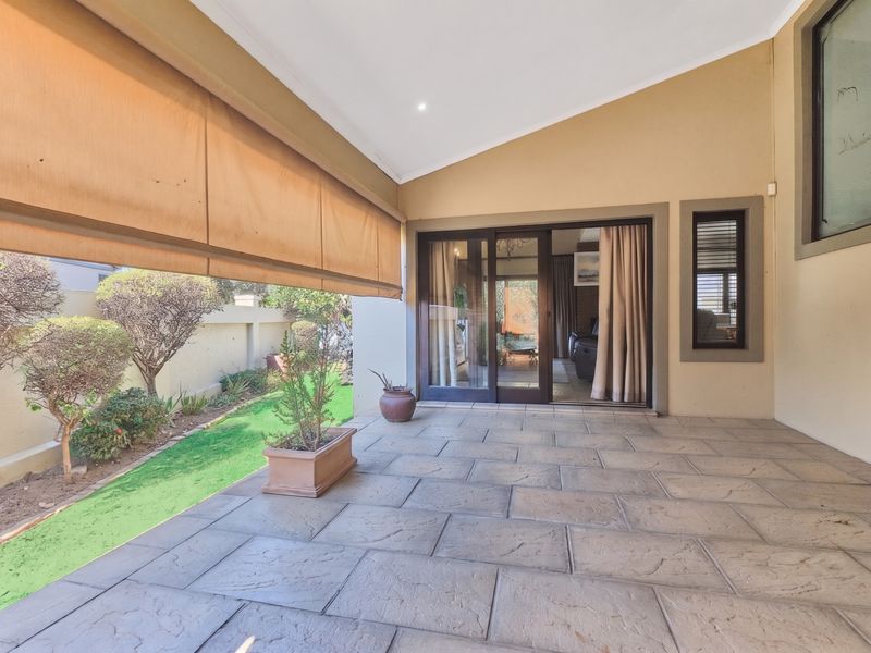 A covered patio area featuring tiled flooring, a retractable outdoor blind, and sliding glass door access to the interior living space.