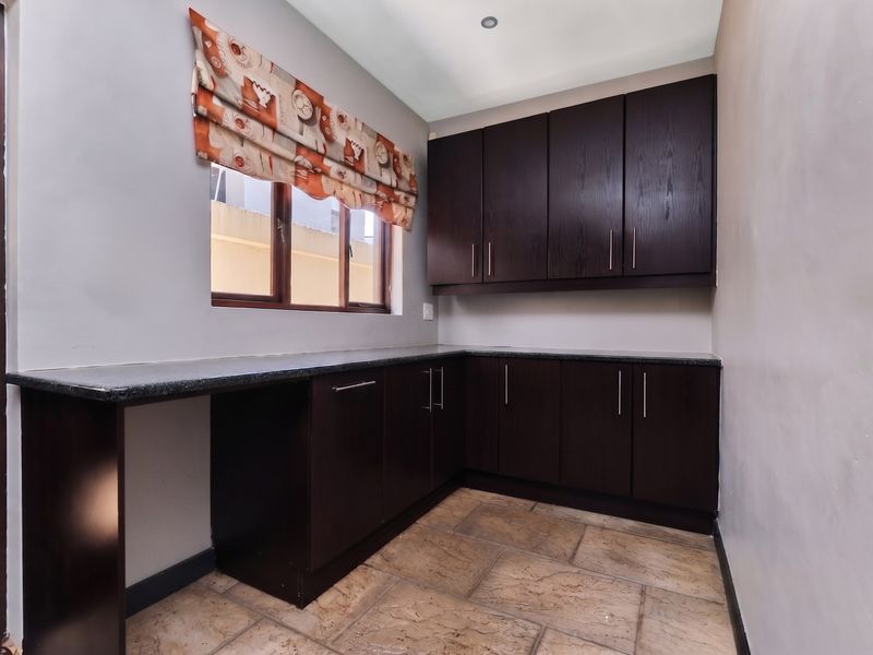 A functional scullery featuring dark wood cabinetry, granite countertops, and tiled flooring, providing ample storage and workspace.