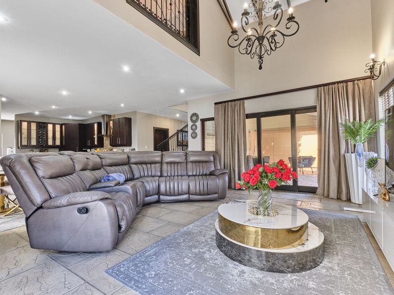 Spacious open-plan living area featuring high ceilings, a mezzanine level with wrought iron balustrade, tiled flooring, and seamless access to the outdoor patio.