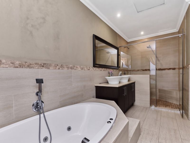 Modern bathroom featuring a jetted bathtub, dual vessel sinks on a dark vanity, and a spacious walk-in shower with glass enclosure.