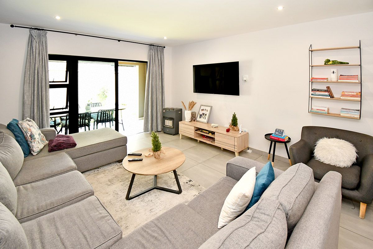 A bright and modern living room featuring large sliding glass doors that open onto a patio, tiled flooring, and recessed ceiling lighting.