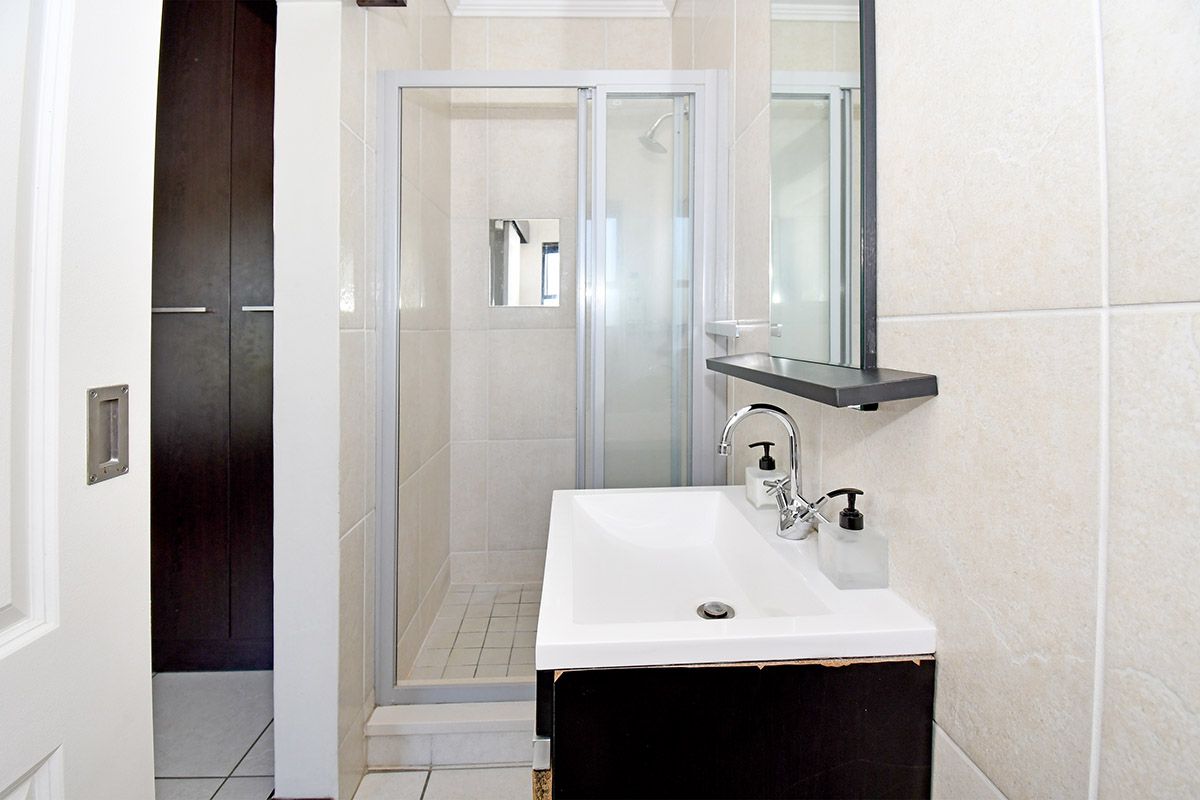 A compact bathroom featuring a glass-enclosed shower, a modern wall-mounted basin with chrome faucet, and built-in storage cabinetry.