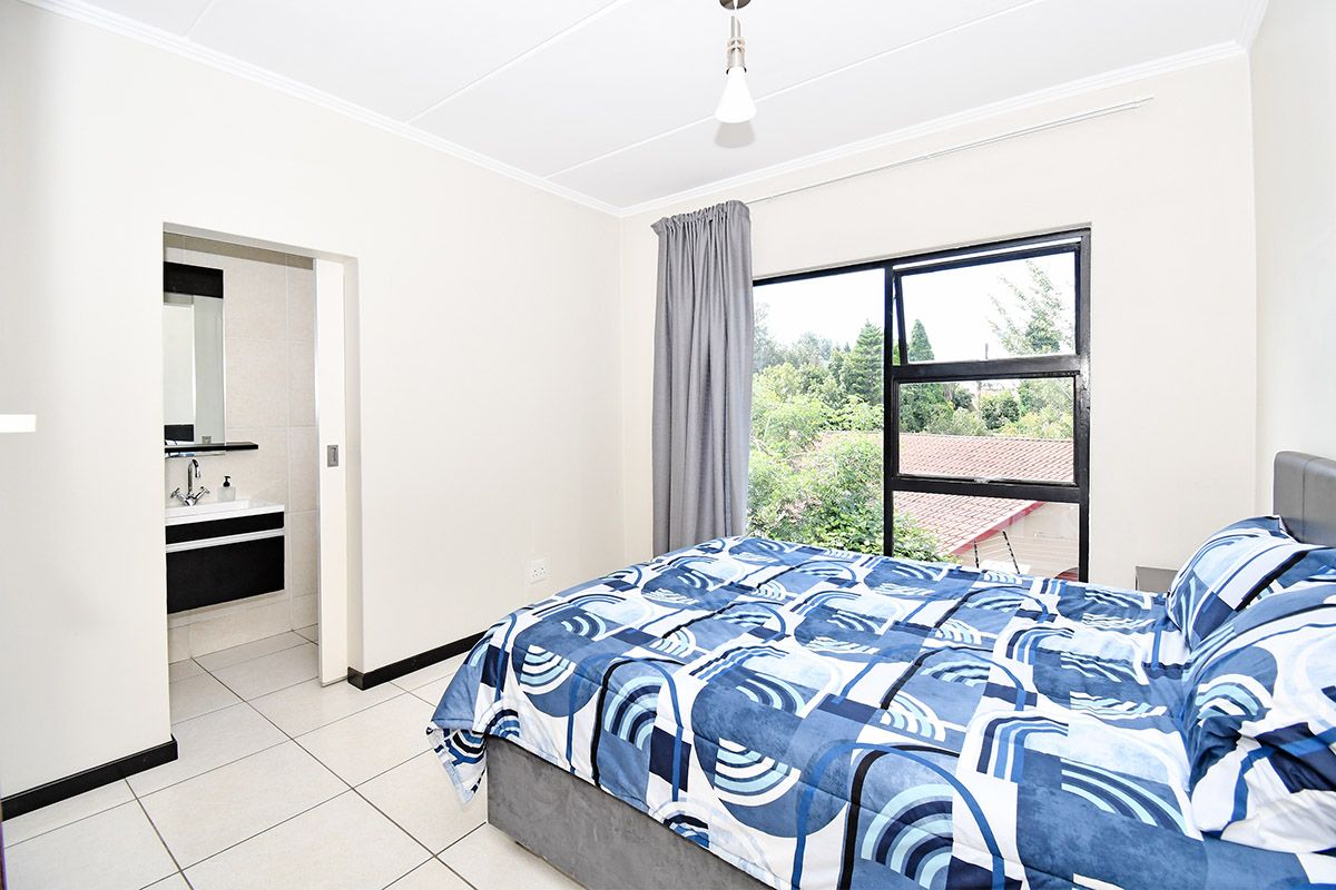 A bright bedroom featuring tiled flooring, a large window with natural light, and an en-suite bathroom with a modern vanity.