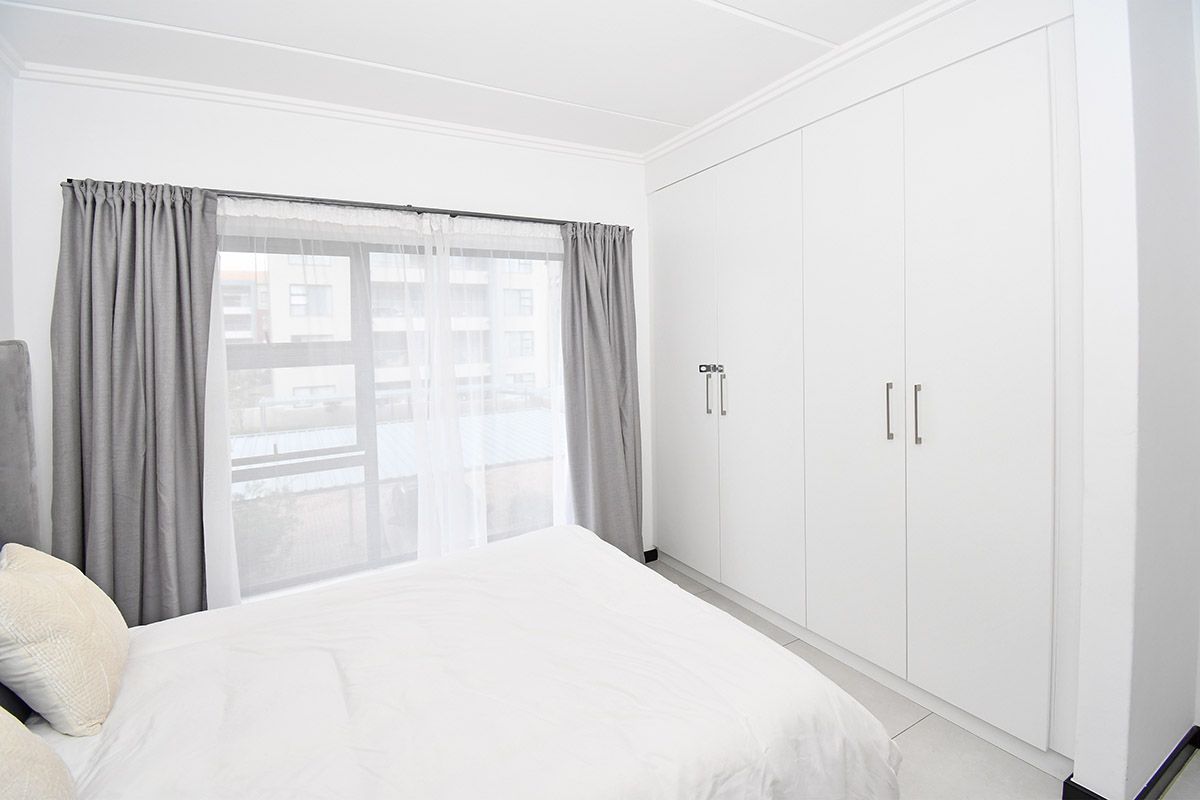 A bright and well-maintained bedroom featuring extensive built-in cupboards, neutral tiled flooring, and large windows allowing for ample natural light.