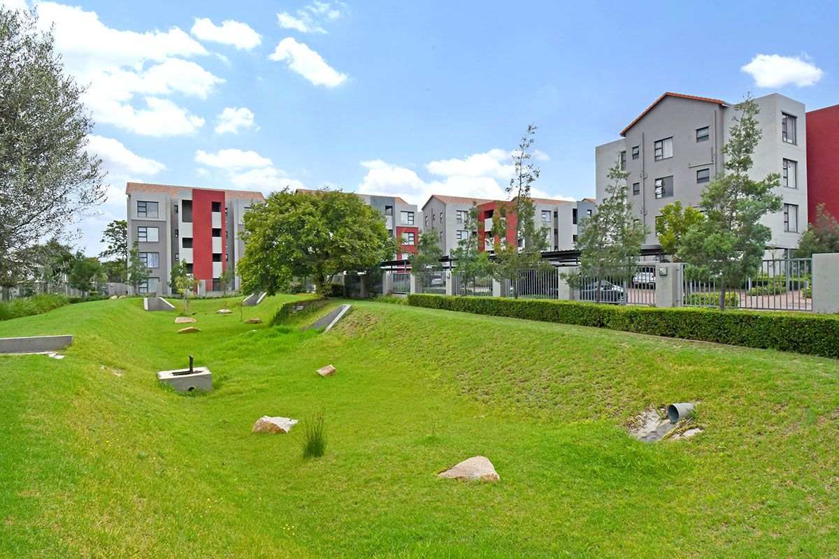 A view of the apartment complex exterior featuring landscaped green spaces, manicured hedges, and secure perimeter fencing.