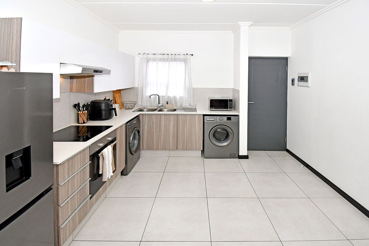Modern kitchen featuring sleek wood-grain and white cabinetry, integrated appliances, electric hob, oven, and tiled flooring in a clean, functional layout.