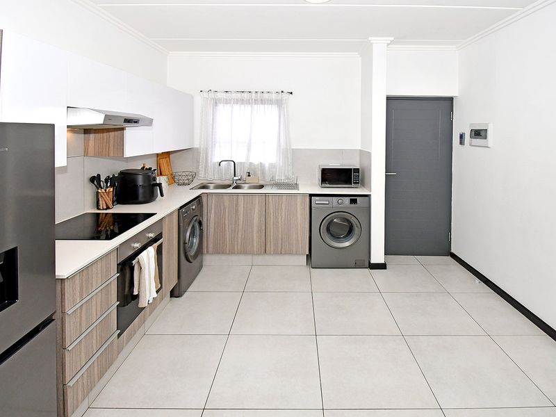 Modern kitchen featuring sleek wood-grain and white cabinetry, integrated appliances, electric hob, oven, and tiled flooring in a clean, functional layout.