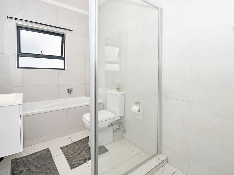 A modern, well-maintained bathroom featuring a built-in bathtub, a separate glass-enclosed shower, a toilet, and a vanity cabinet with neutral tiled finishes.