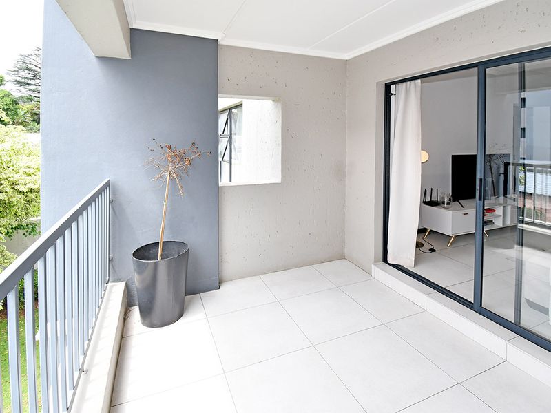 A clean, modern balcony featuring tiled flooring, a metal balustrade, and large sliding glass doors providing seamless access to the interior living space.