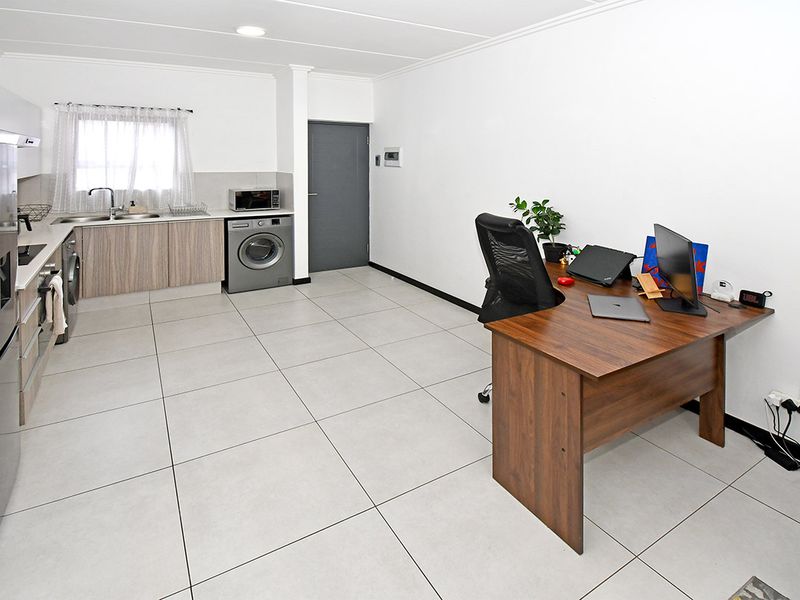 Modern open-plan apartment featuring a functional kitchen area with built-in cabinetry and tiled flooring, seamlessly integrated with a versatile living or workspace.
