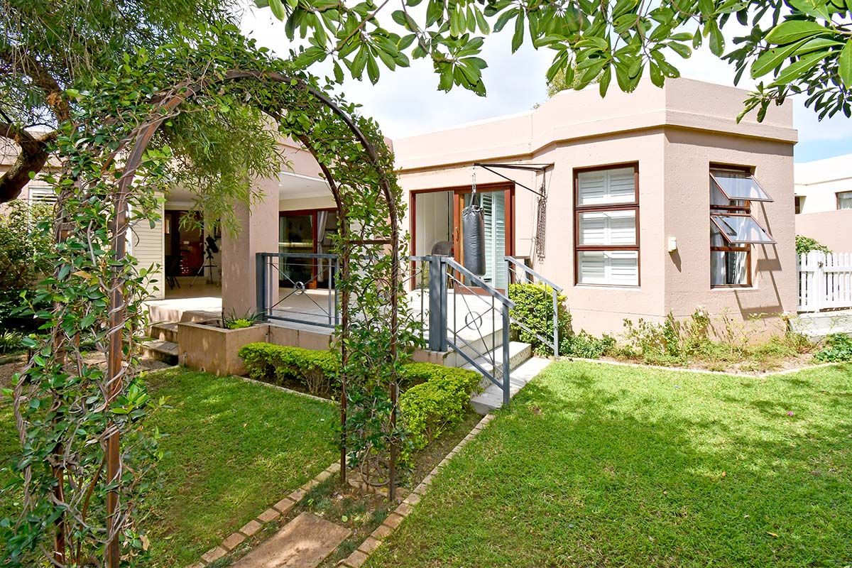 Rear view of the property featuring a covered patio, landscaped garden, metal garden arch, and sliding glass doors leading into the home.