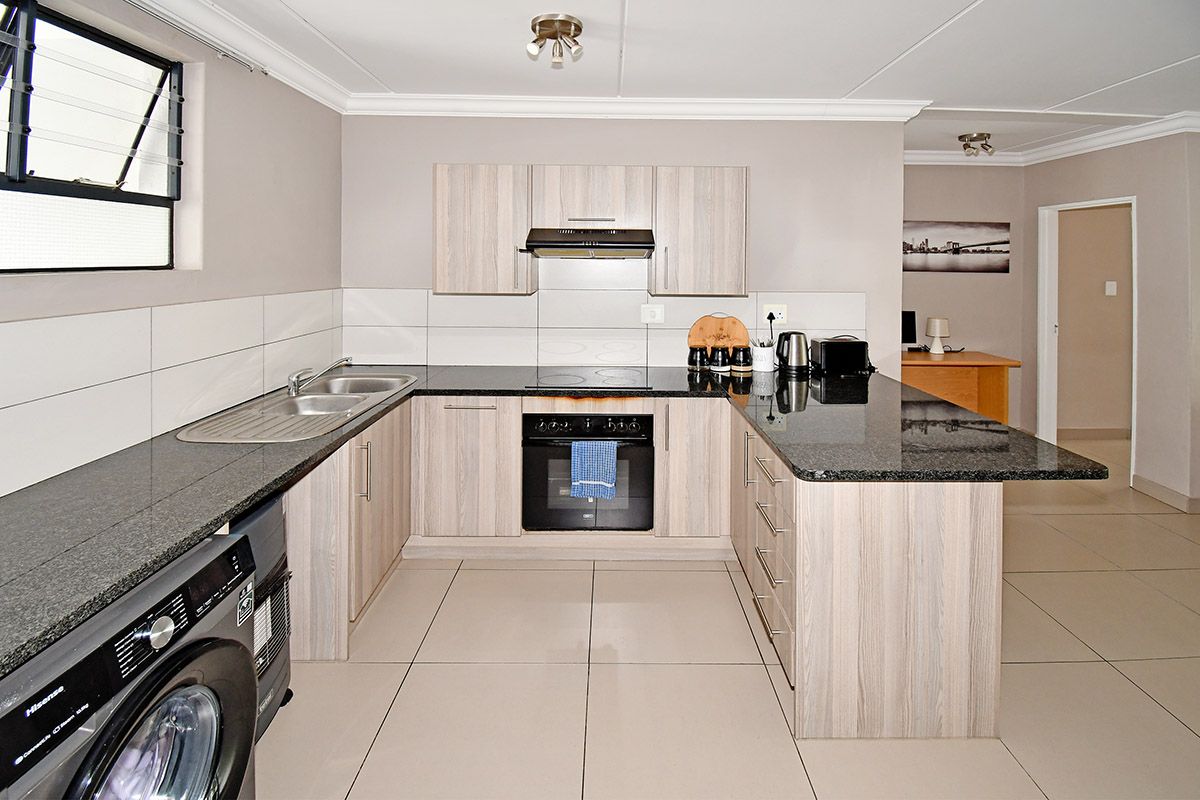 Modern kitchen featuring light wood-grain cabinetry, granite countertops, integrated oven, hob, extractor fan, and a double sink with tiled splashbacks.