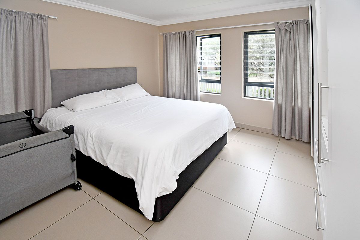 A well-lit bedroom featuring neutral tiled flooring, built-in cupboards, and large windows with security louvers.