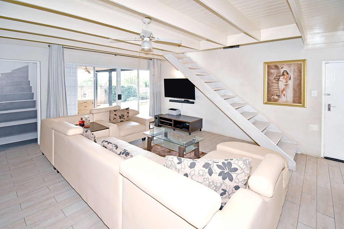 Spacious living area featuring exposed beam ceilings, a built-in staircase, and large sliding glass doors providing access to the outdoor patio.