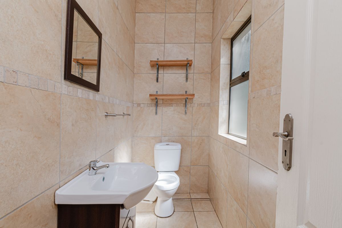 A compact, fully tiled guest bathroom featuring a modern vanity basin, toilet, and frosted glass window for privacy.