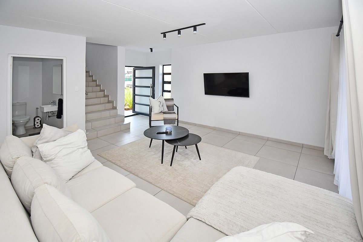 Modern open-plan living area featuring neutral tiled flooring, track lighting, and direct access to a guest bathroom and staircase.