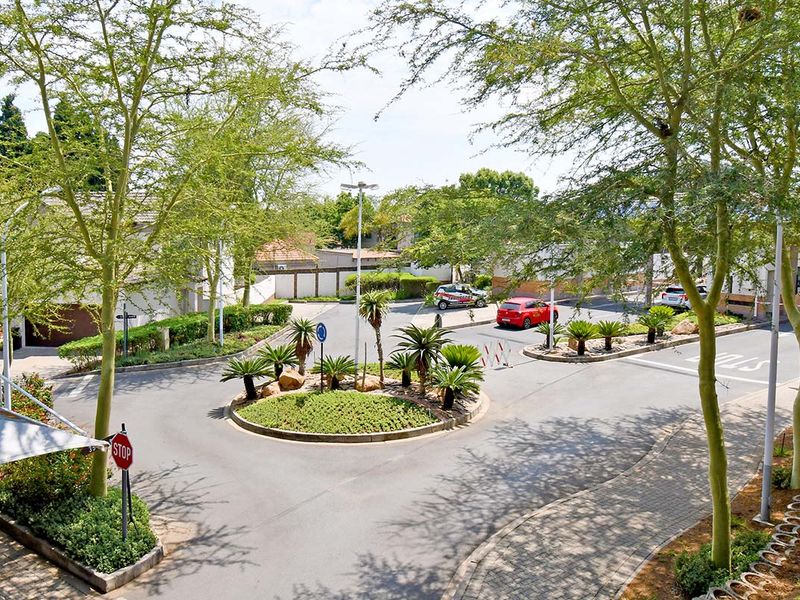 An elevated view of the complex entrance featuring a landscaped roundabout, paved walkways, and established trees within a well-maintained residential estate.